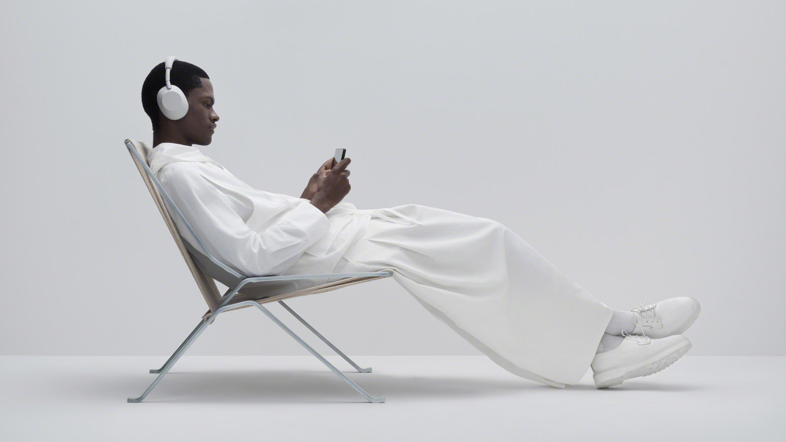 A man sitting in a chair, dressed in all white and wearing a white pair of Sony WH-1000XM6 headphones.