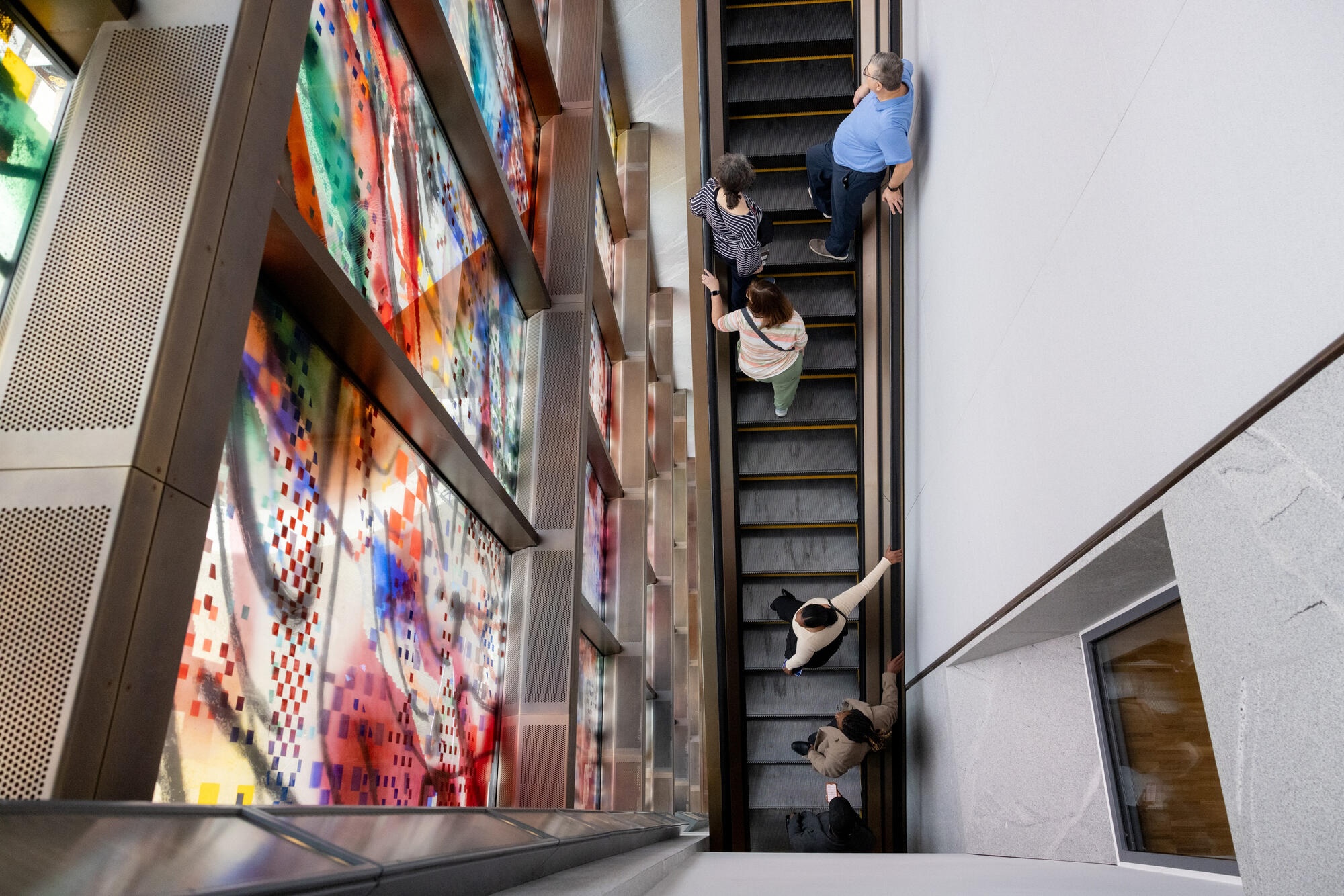 inside obama presidential center with an escalator ascending alongside a colorful stained glass artwork