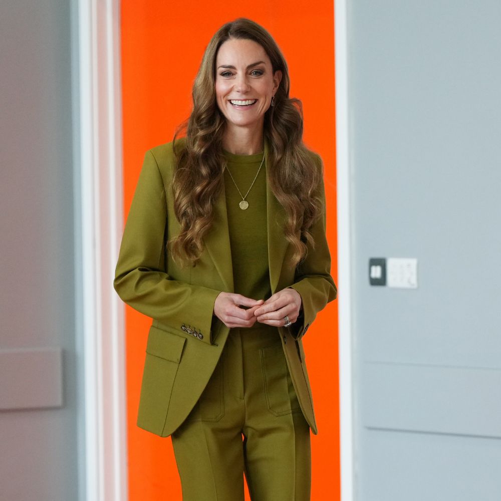 Kate Middleton wears an olive green suit set with light brown pointe-toe heels and a gold pendant necklace.