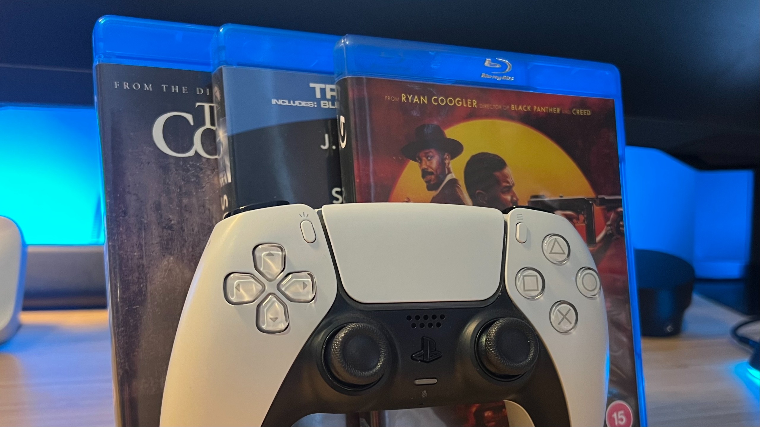 Blu-Ray cases lined up behind a white PS5 DualSense controller
