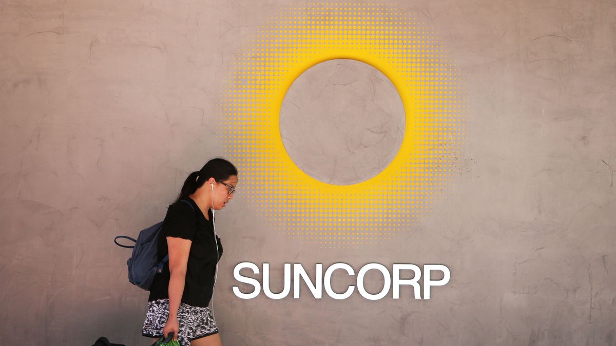 Suncorp logo on a cement wall with a woman walking in front of it holding shopping bags