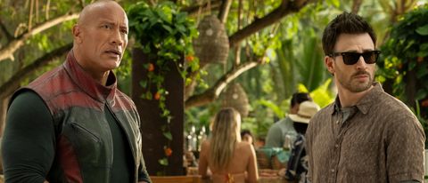 Dwayne Johnson and Chris Evans standing in a tropical setting, staring at something off camera, in Red One.