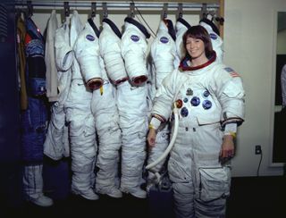 Astronaut Anna Fisher poses in an Apollo spacesuit next to a rack of other spacesuits during training for a Hubble Space Telescope servicing spacewalk in 1980.