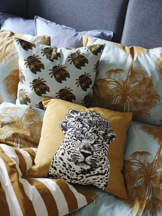 A bed with palm patterned bedding and an orange cushion with a leopard design