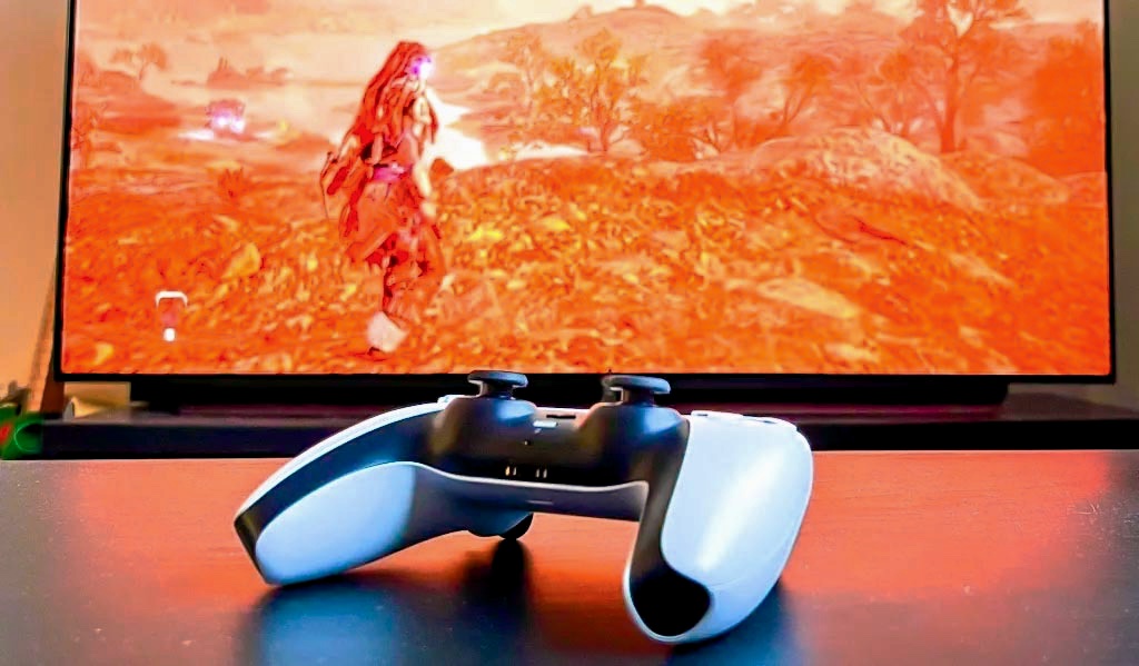 A PS5 DualSense controller in front of Horizon Forbidden West on the screen