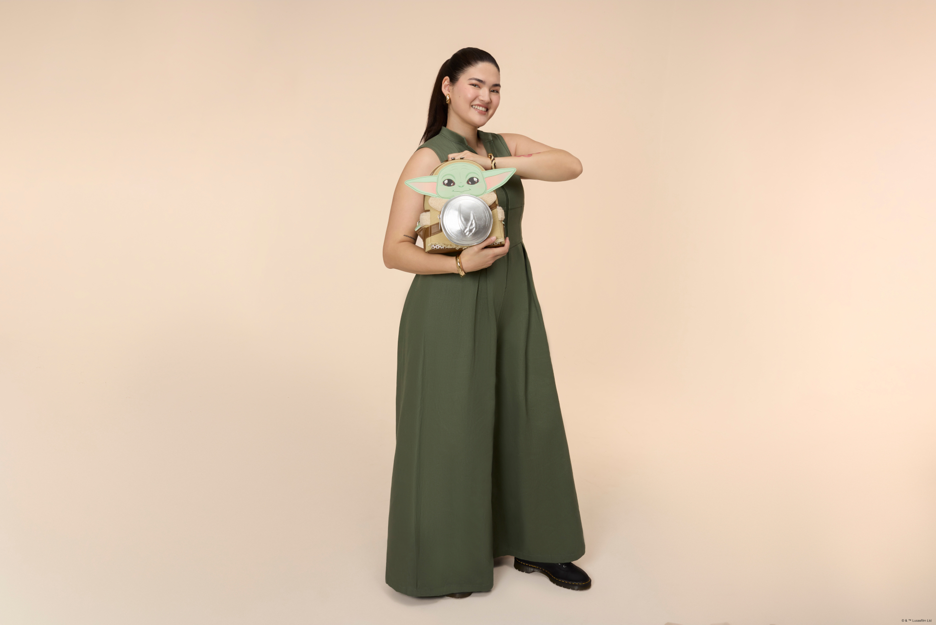 A woman wears a Grogu Loungefly mini-backpack in a pink environment