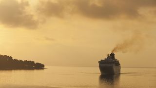 A cruise ship sails off the coast of Corfu with a yellow, smoggy sky.