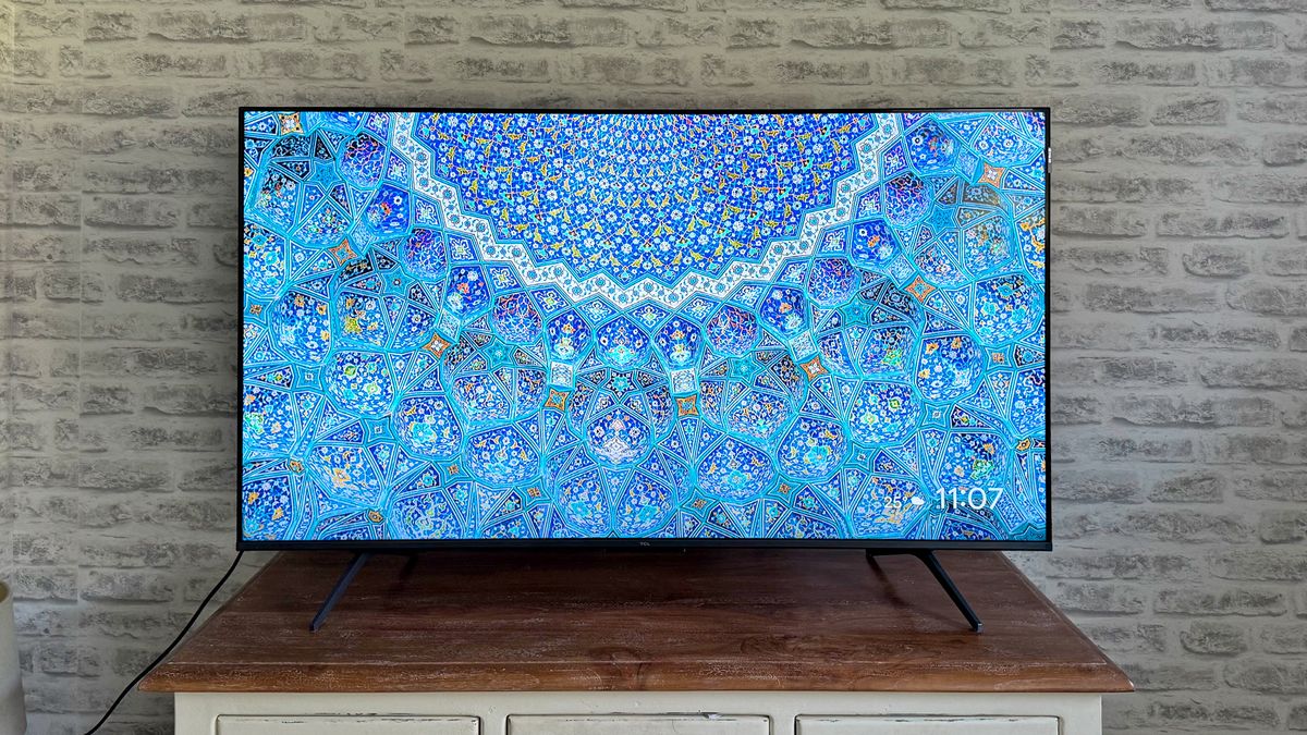 The TCL C6KS 50-inch TV straight-on on a TV cabinet in front of a brick wall. On screen is an intricate blue pattern. This is our pick for best cheap TV.
