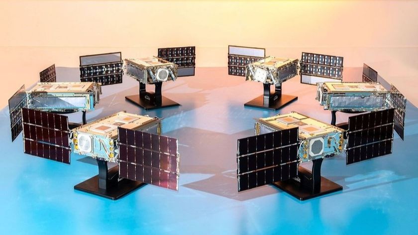 six small satellites with solar panels deployed stand in a circle on a table facing inward.