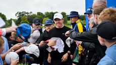 Rory McIlroy walks through a crowd of fans with a plethora of hats and pens stretched out in his direction at the 2025 Irish Open