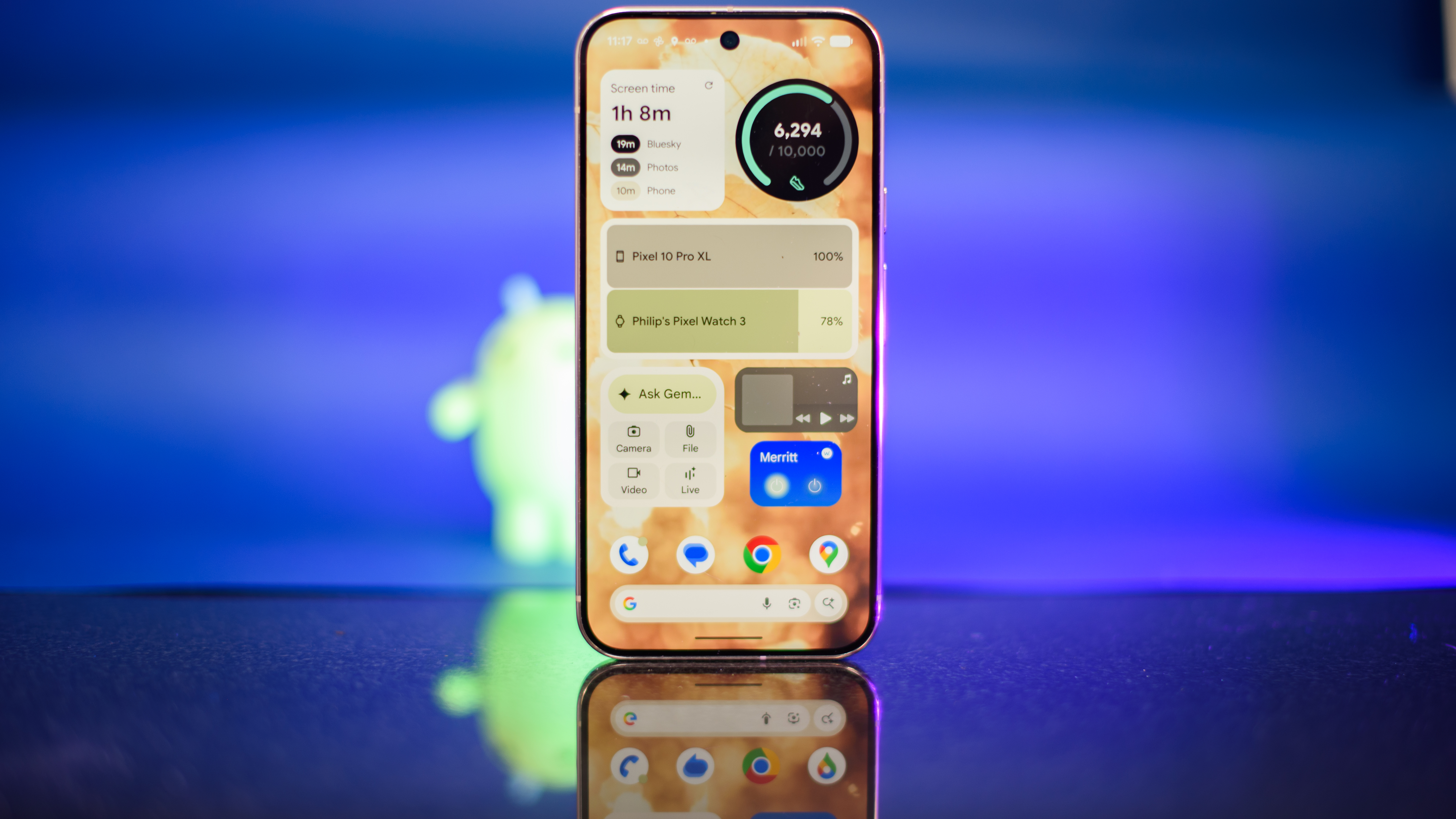 Google Pixel 10 Pro XL in Porcelain against a blue background with a green neon Android figurine in the background