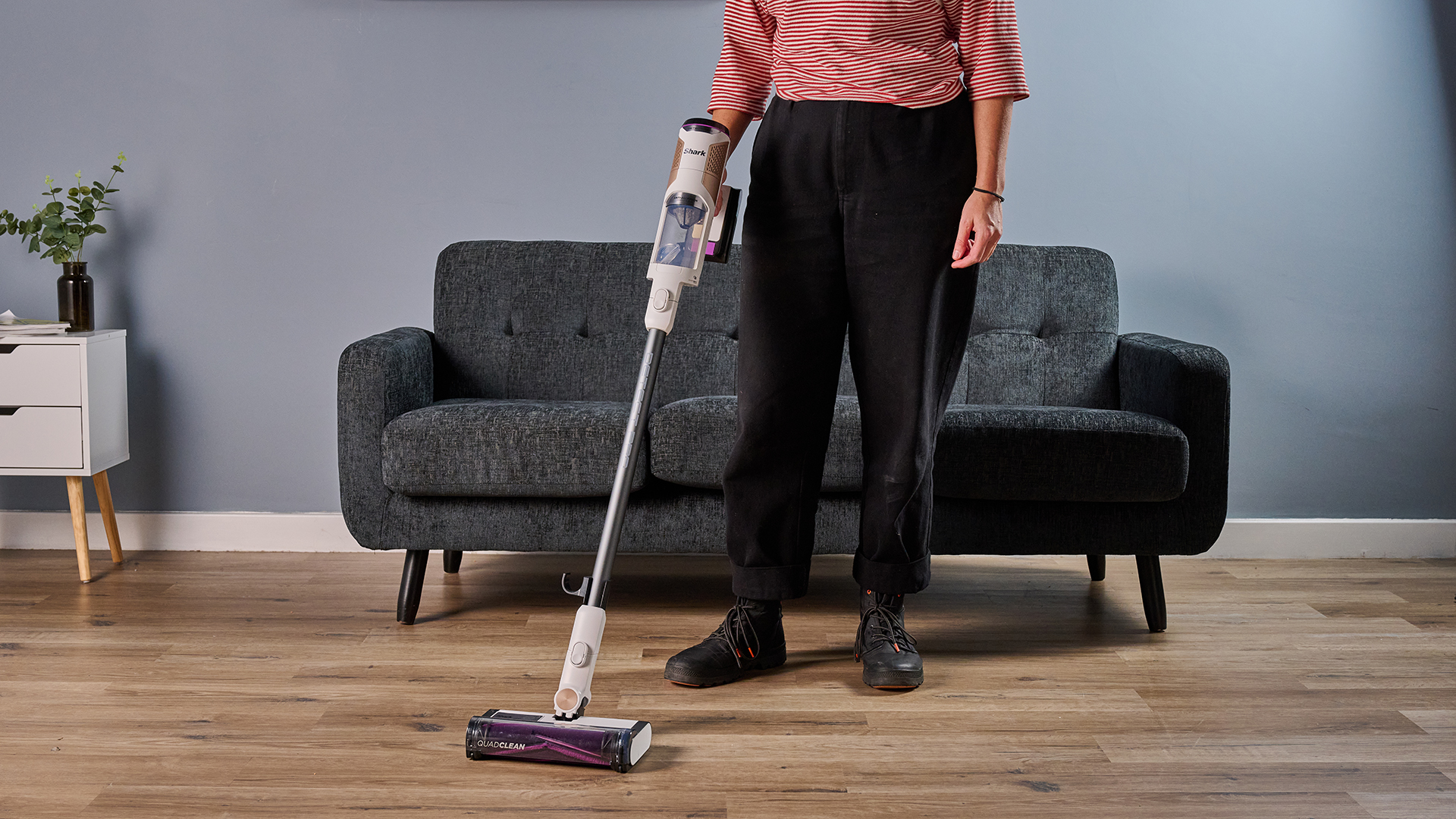 Ruth Hamilton holding Shark Detect Pro Cordless cordless stick vacuum, with a sofa and side table in the background