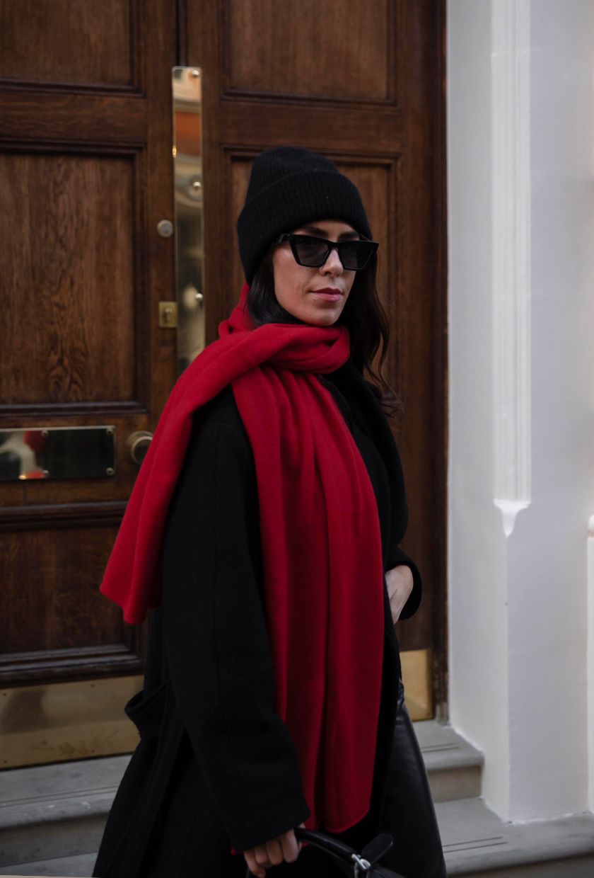 Jessica Skye wears a black beanie and jumper with a red scarf, one of the best autumn fashion colour combinations.