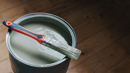 An open tin of paint with a paint brush 