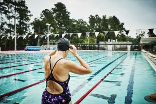 A woman at an open outdoor swimming pool adjusting goggles at side of pool