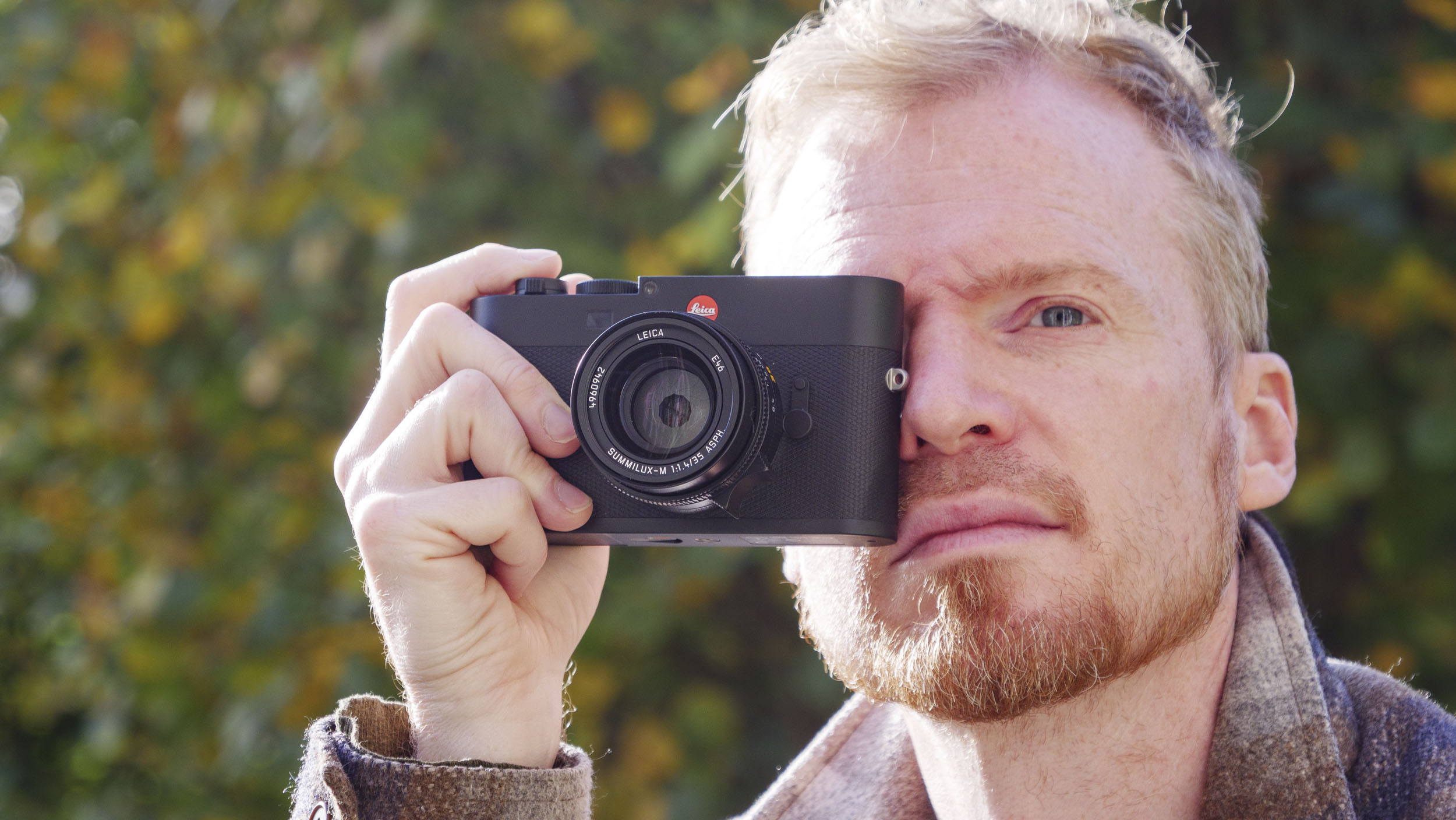 Man holding the Leica M EV1 camera's viewfinder up to their eye, autumn leaf backdrop