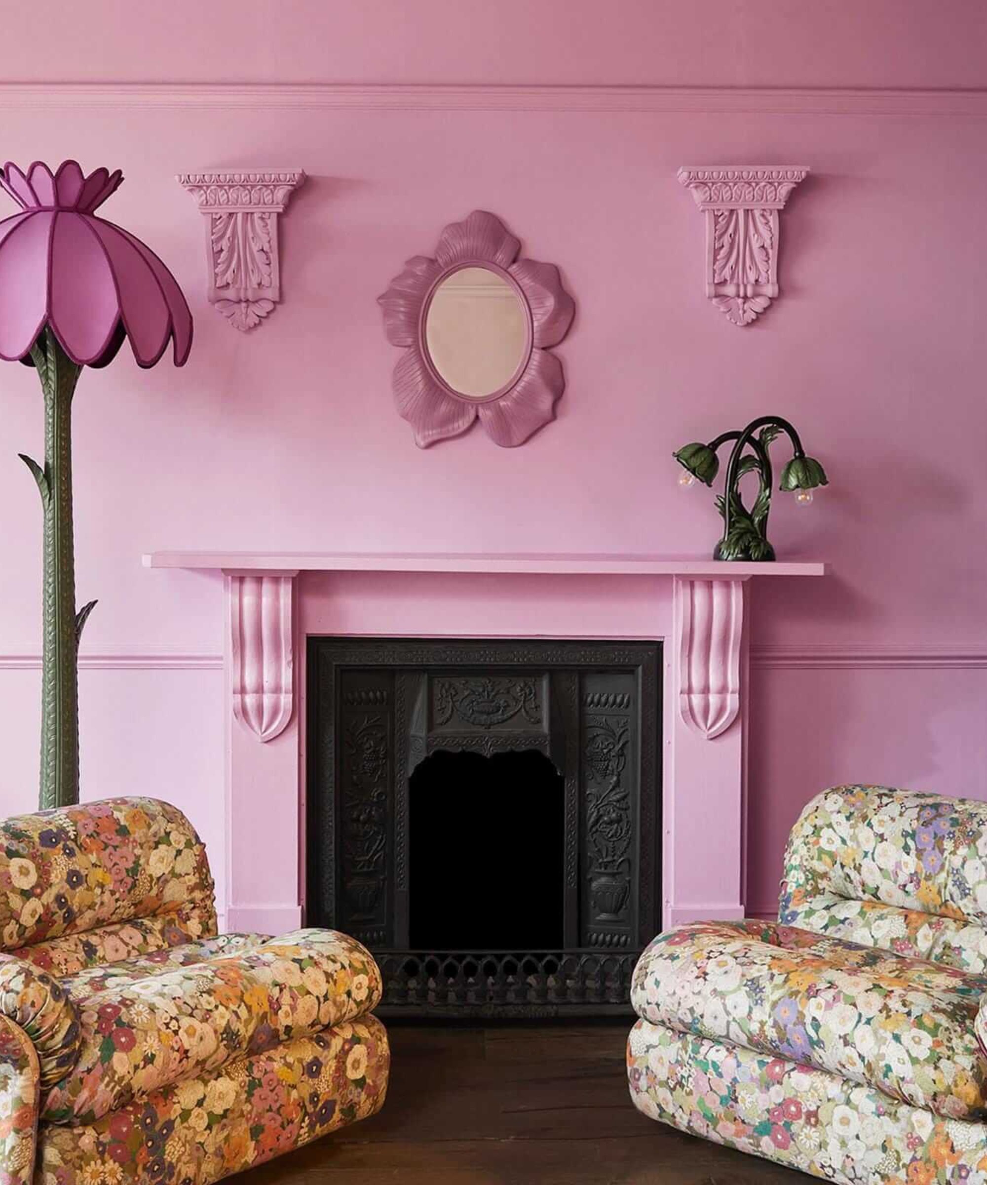 A sitting room painted in bright barbie pink, with two retro style floral chairs and a lamp shaped like a flower