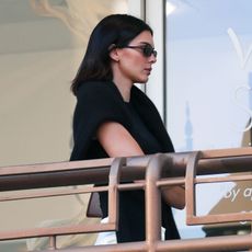 Kendall Jenner walks outside sushi park wearing a black top with a black jumper knotted around her shoulders and cream satin trousers.