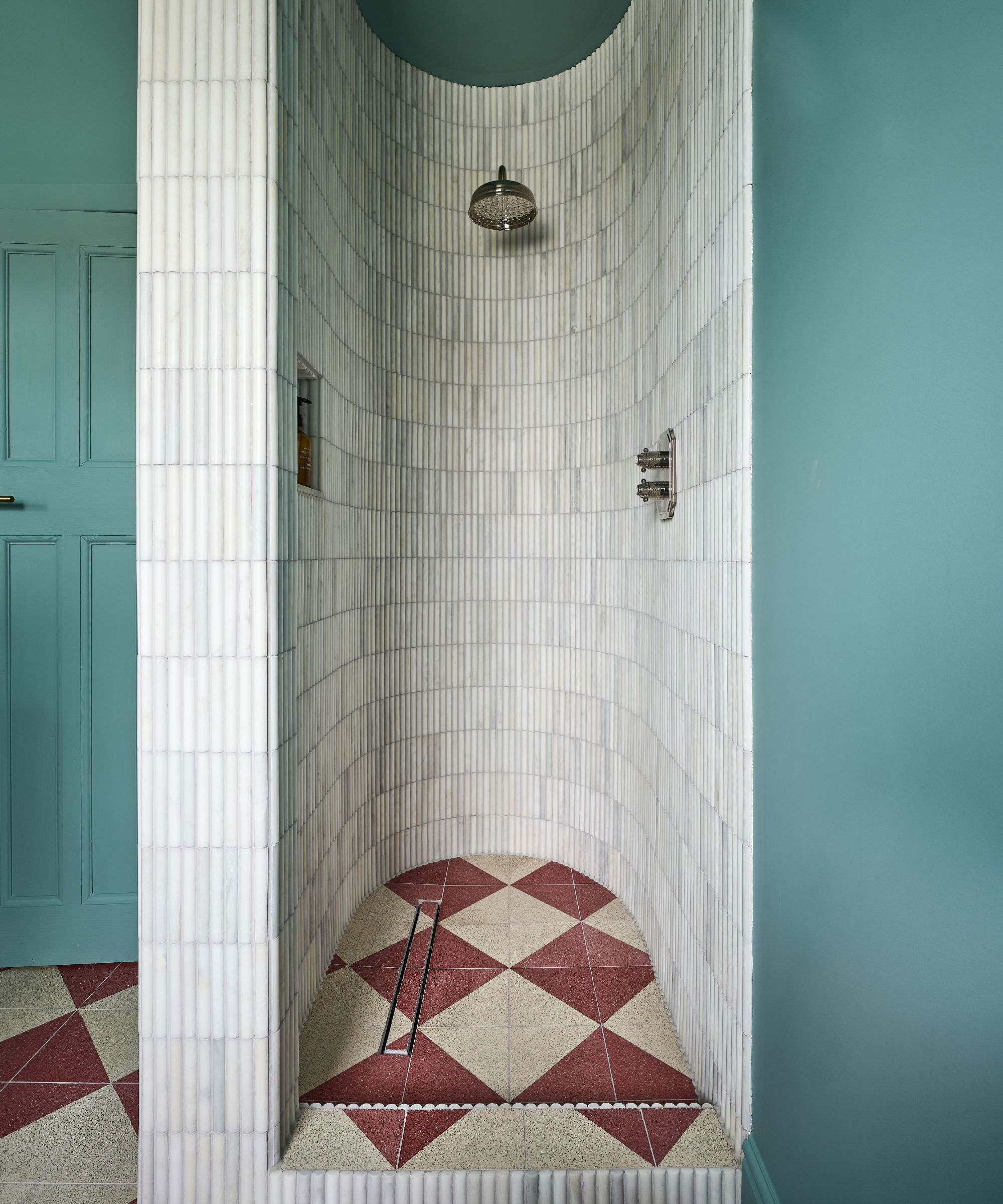 Blue bathroom with red diamond tile flooring and small white mosaic curved shower