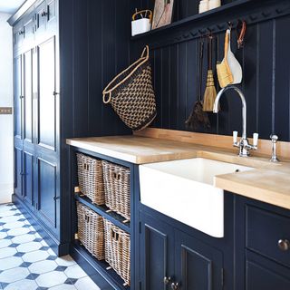 Navy kitchen utility room with Belfast sink, wicker basket storage and patterned tiled floor