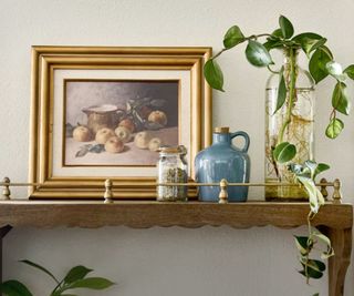 Wooden and brass shelf with still life picture, plant and olive oil