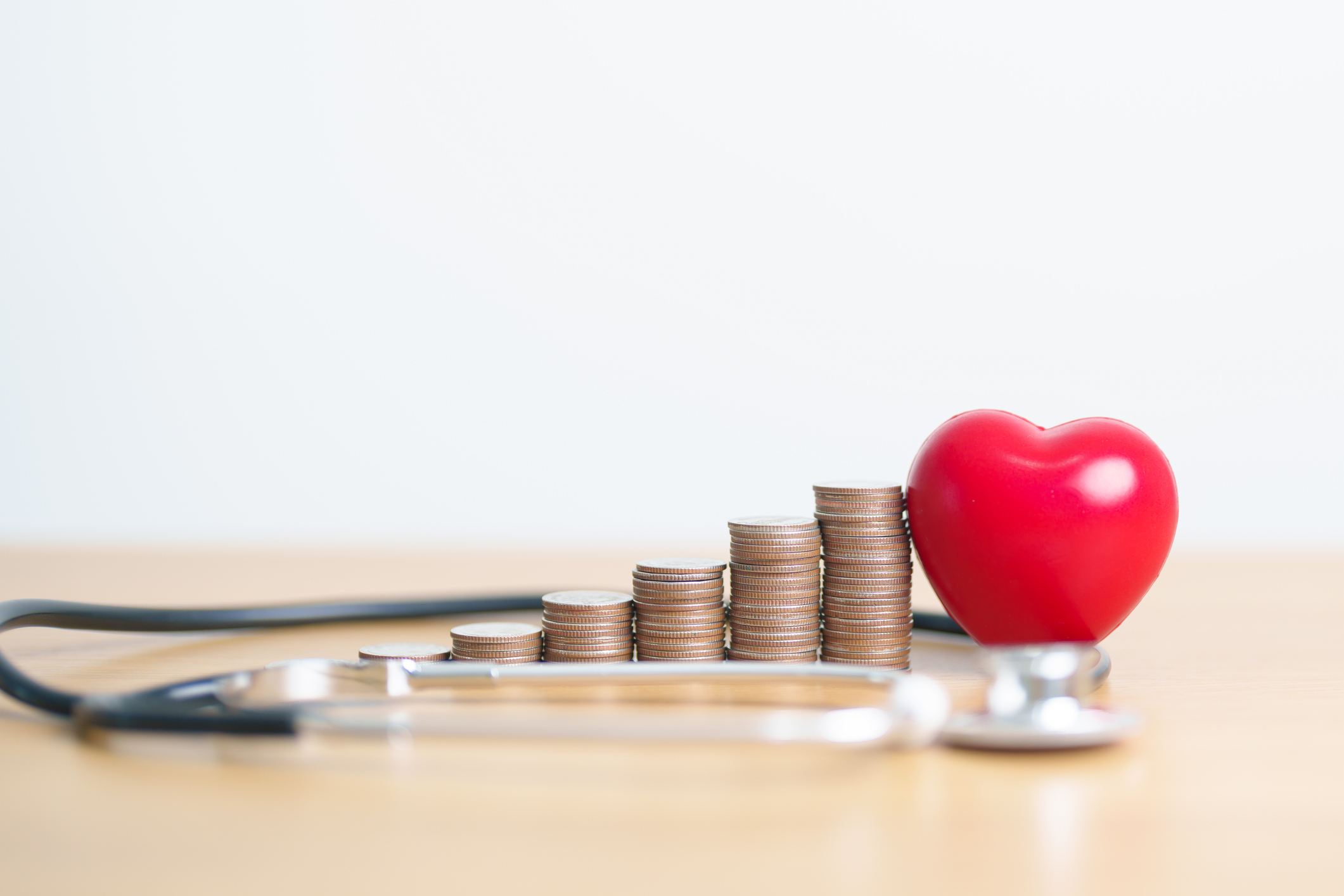 ascending stacks of coins with a stethoscope and red plastic heart