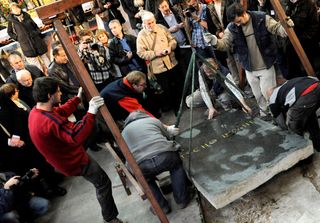 a group of people standing around a small crane. the crane is lifting a stone slab that has the name of tycho brahe on it