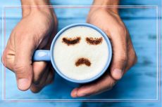 A cup of coffee in a blue mug with a sad face on top