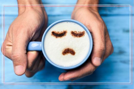 A cup of coffee in a blue mug with a sad face on top