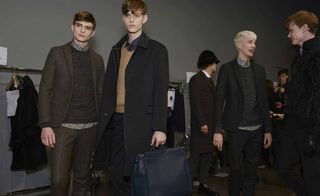 Six male models wearing looks from Fendi's collection. They are wearing blue, brown, grey and black trousers, shirts, sweaters, coats and jackets. One model is holding a blue bag and another is wearing a black fur hat