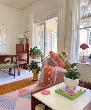 A small living room with plants, a pink chair, and a coffee table