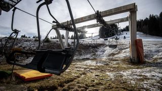 A ski lift without passengers sits on a hillside with little snow