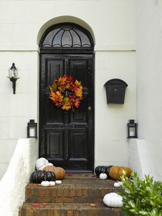 black front door with autumnal wreath and pumpkins