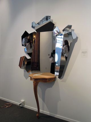 View of 'Skin Louis XV' by Arik Levy - a small wooden console style table with one leg and a large asymmetric mirror above it