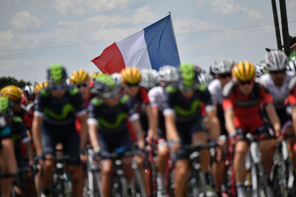 The French flag waves behind the Tour de France peloton.