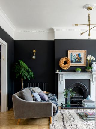 A black living room with dark fireplace decor, dark wall paint decor, grey sofa, parquet-effect flooring, berber-style rug and metal coffee table