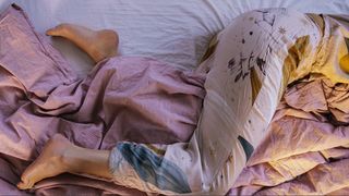 Woman's legs in pink patterned pyjamas on top of bedding.