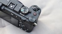 Close-up of a black digital camera's top controls including mode dial, shutter button, on/off switch, and menu buttons