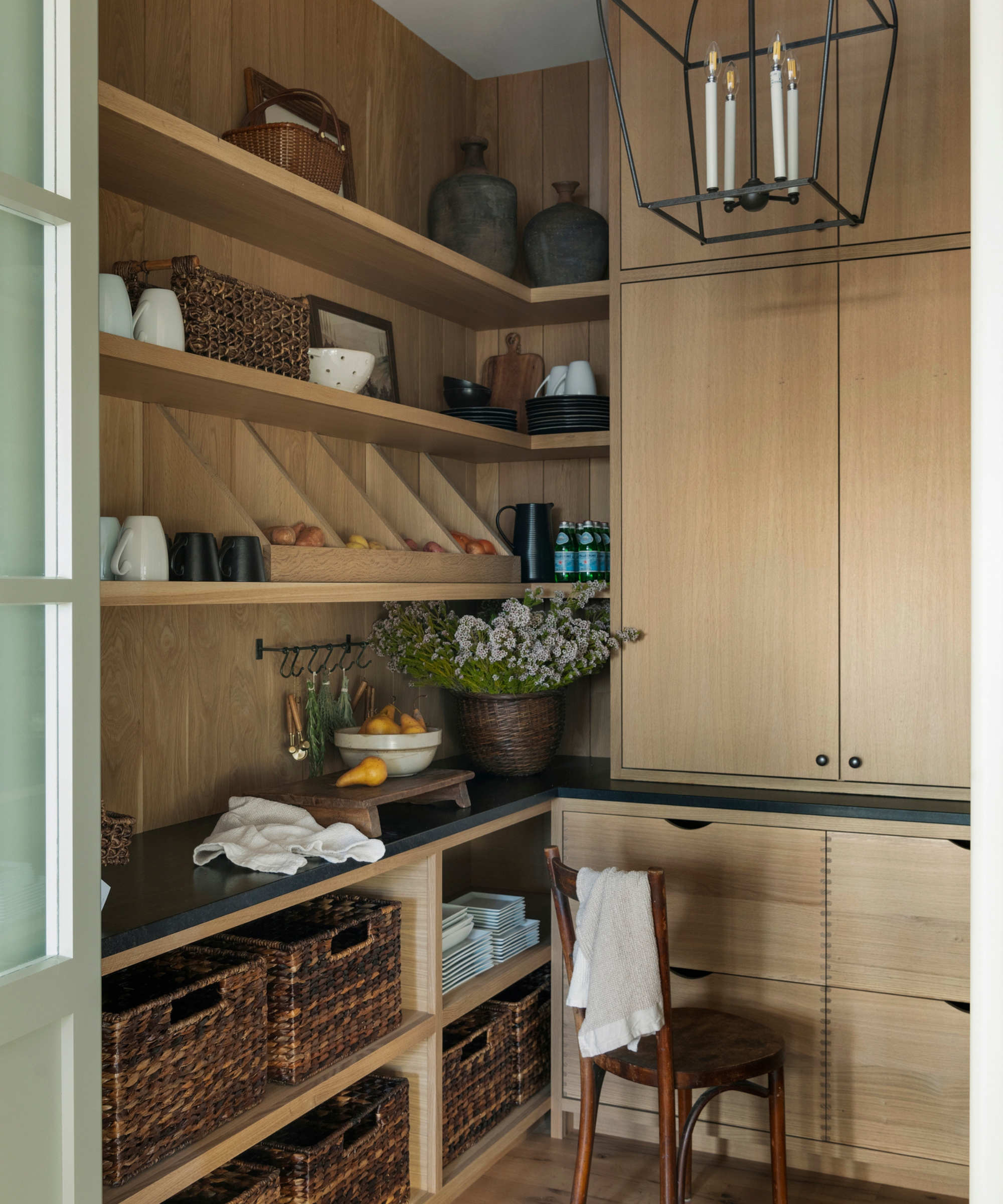 A wooden pantry with black countertops and a mix of open and closed storage, including woven baskets