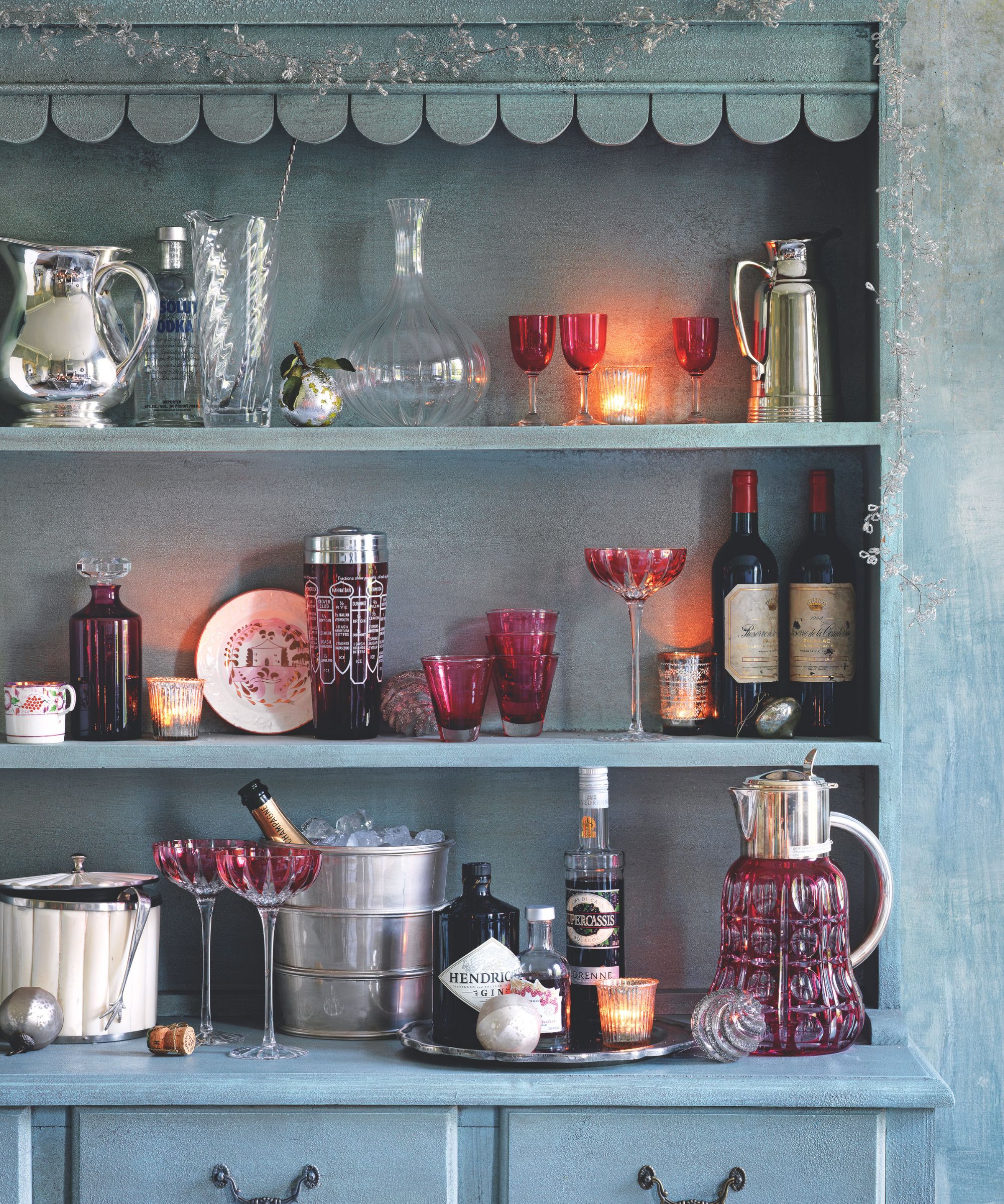 Christmas drinks bar on a dresser with red glassware, pitchers, bottles and ice buckets