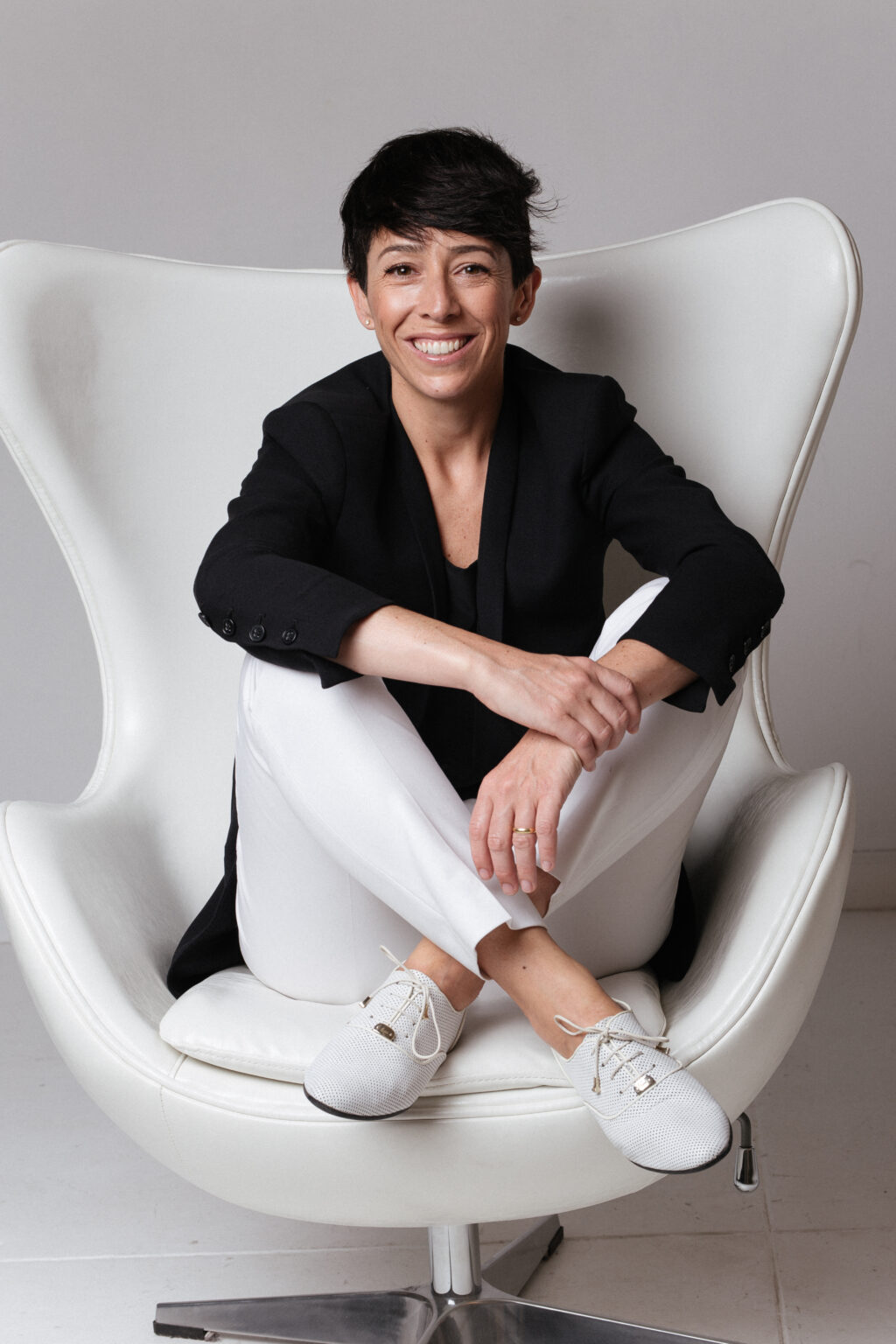 A woman with cropped brown hair sitting cross-legged in a chair