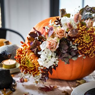 pumpkin table centrepiece filled with flowers and a small tealight candle sitting alongside