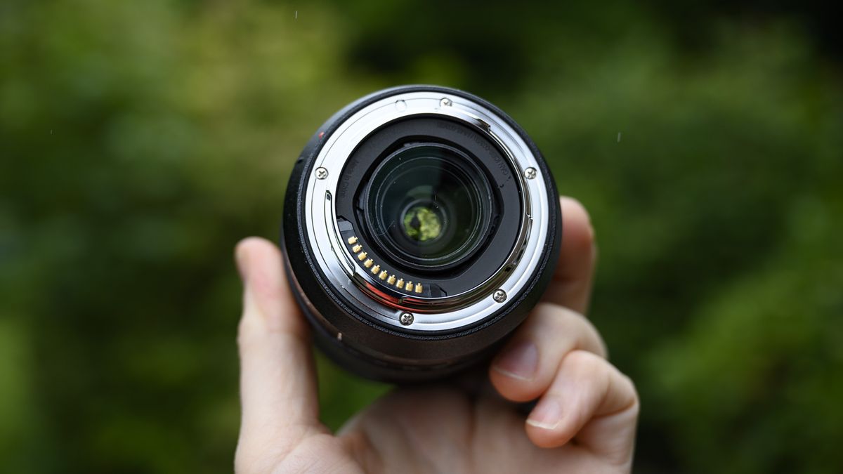 Panasonic Lumix S 28-200mm travel lens in the hand with leafy background and light rain