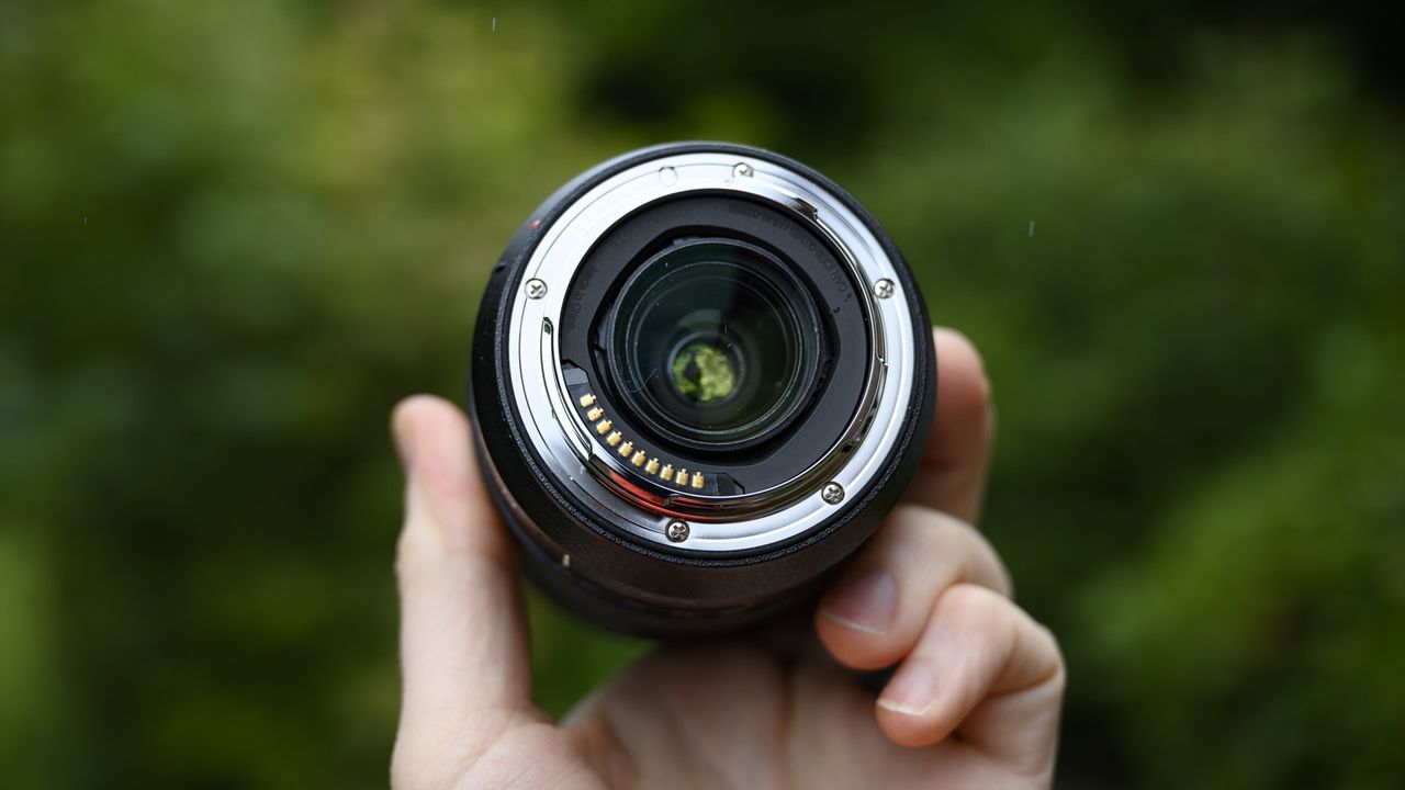 Panasonic Lumix S 28-200mm travel lens in the hand with leafy background and light rain