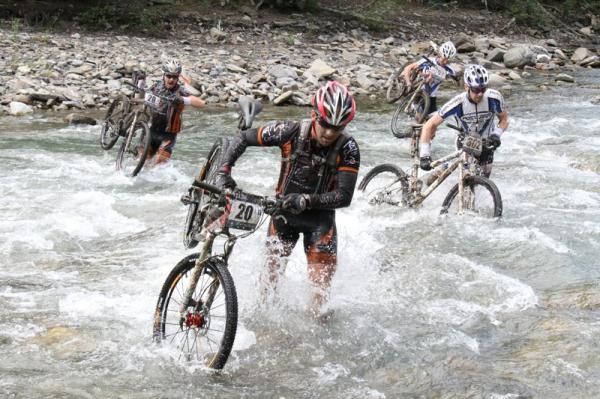 East meets west as Team Nativo Concept (number 20) from Quebec fords a river with team Frontrunners/Kona from BC (number 302)