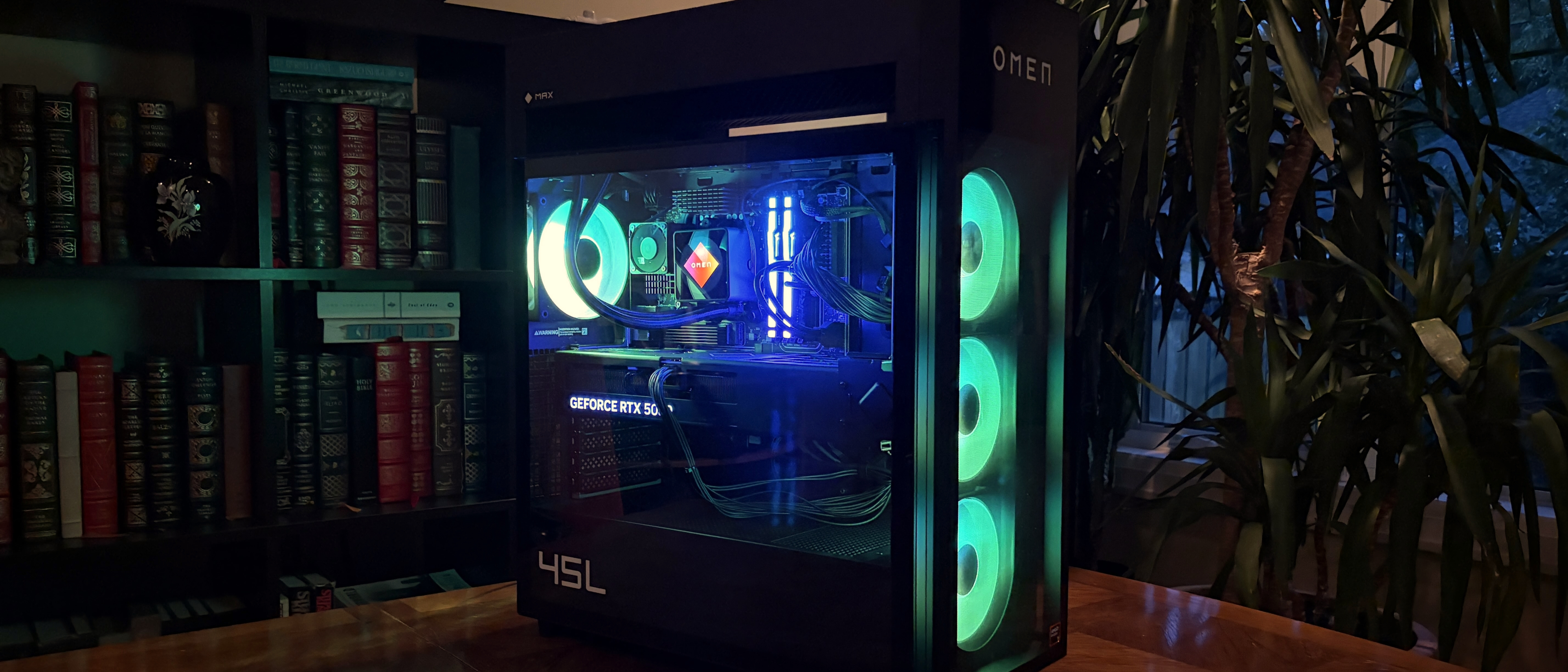 A modern HP Omen Max 45L gaming PC case with illuminated cooling fans and colorful internal components, placed beside a bookshelf and indoor plants.