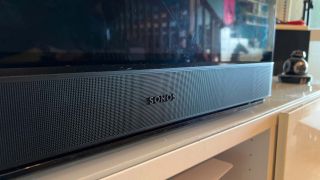 En svart Sonos Beam gen 2 ligger på en träfärgad TV-bänk.