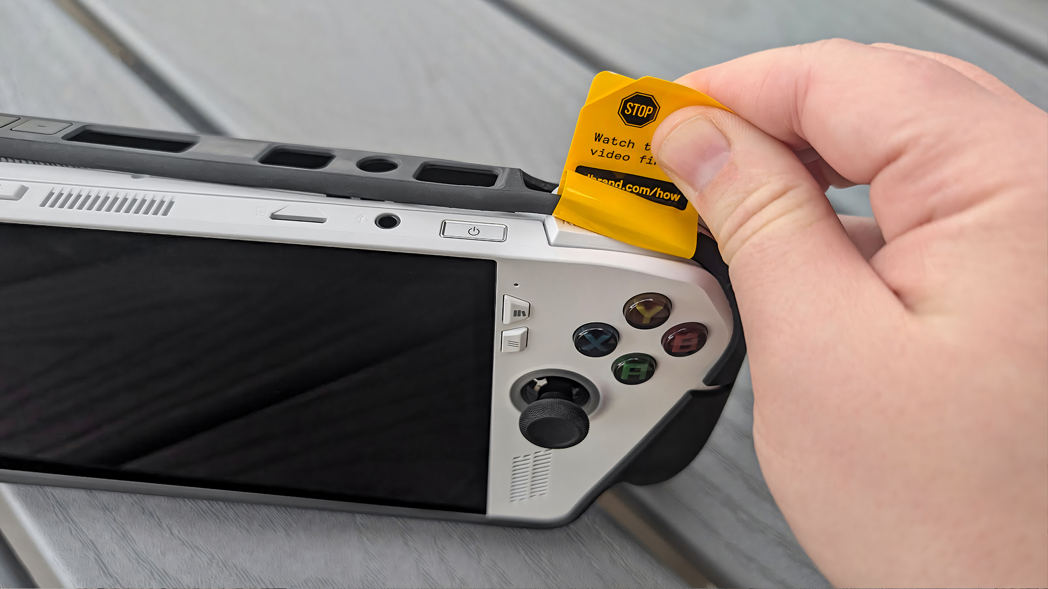 A hand pulling on a yellow installation sticker looped around the top of the dBrand Killswitch.