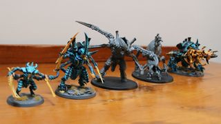 A selection of new and old Warhammer 40,000 Tyranid miniatures set out in a row on a wooden table
