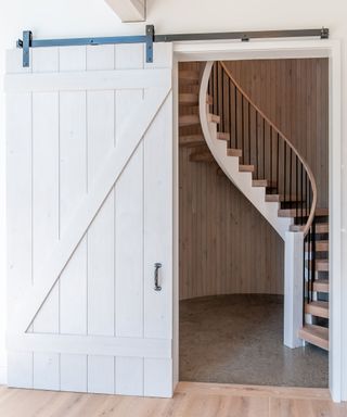 A white barn door opening up to a spiral staircase